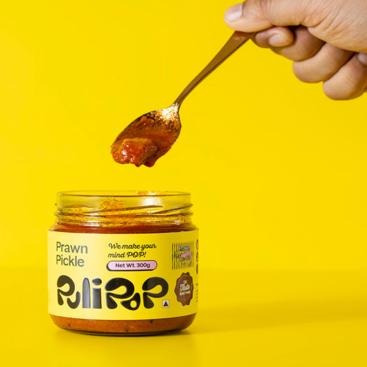Hand scooping spiced prawn pickle from open PuliPOP jar on yellow background