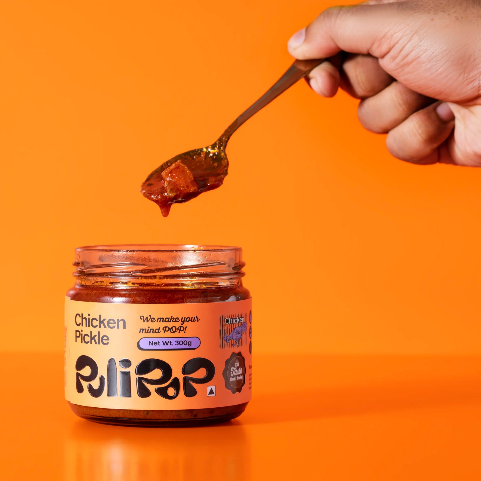 Hand scooping boneless chicken pickle from open PuliPOP jar on orange background