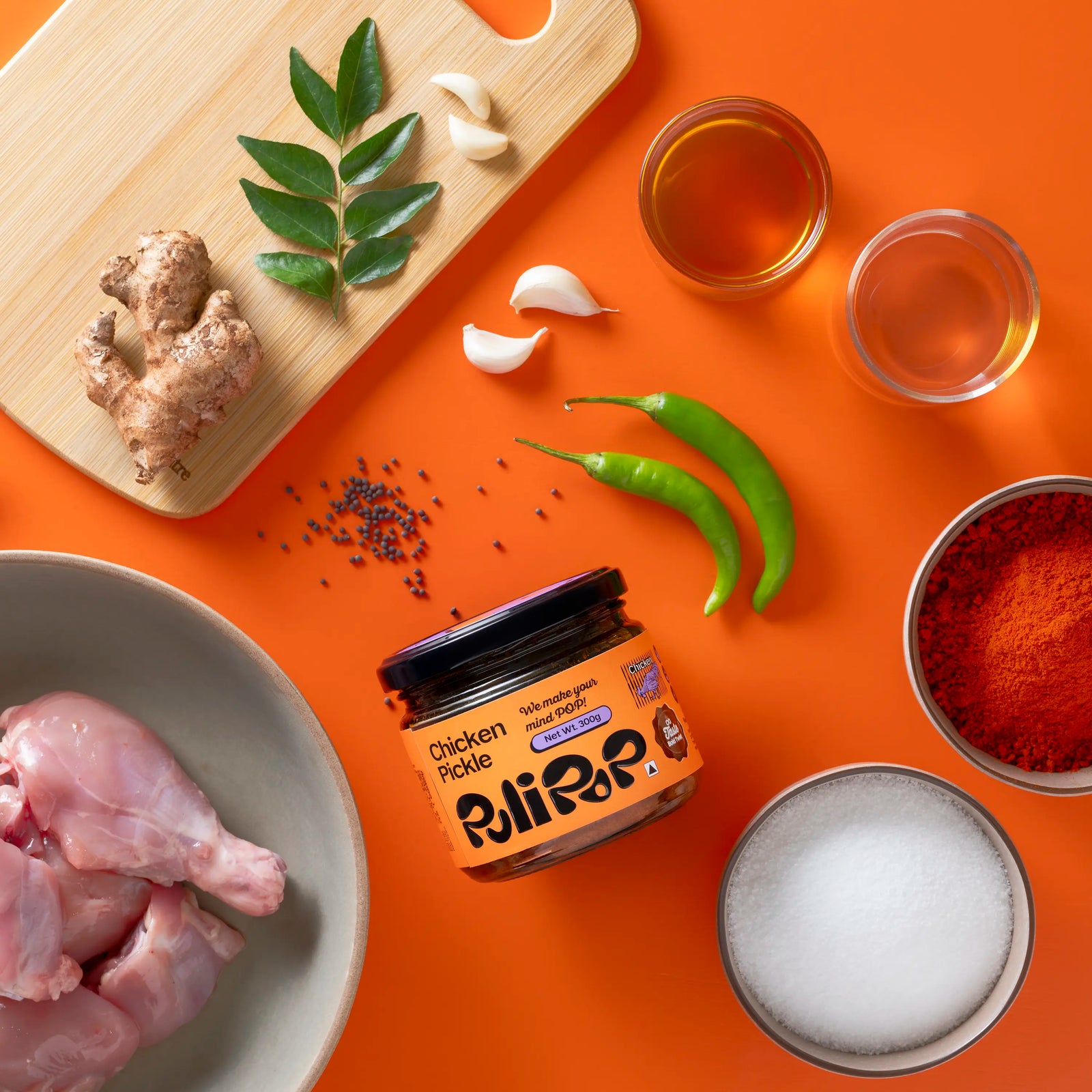Chicken Pickle by PuliPOP surrounded by raw chicken pieces, green chillies, gingelly oil and spices